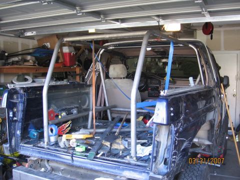 1994 Ford Bronco - This blue SUV is being modified with a custom roll cage, with tools and equipment visible in the bed.