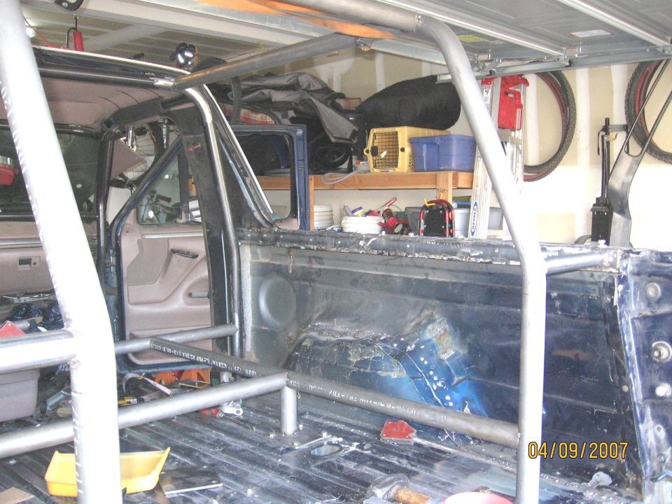 Dark blue Ford Bronco interior with a custom roll cage, showing the rear bed and driver's side door