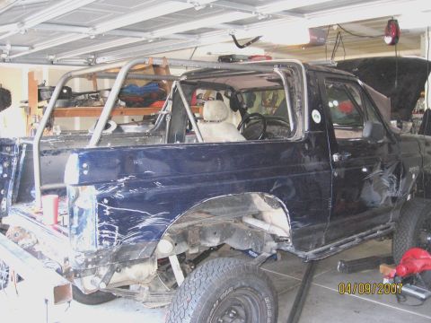 1994 Ford Bronco - This dark blue SUV, possibly a Ford Bronco, is undergoing modifications with a prominent custom roll cage visible.