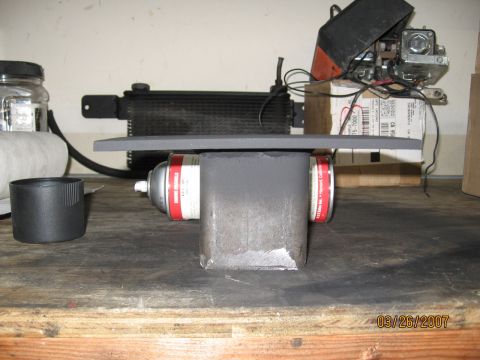 1994 Ford Bronco - A metal bracket is being spray painted with two cans of red and white spray paint on a workbench.