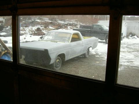 1967 Ford Ranchero - A 1967 Ford Ranchero in primer sits in a lot with snow on the ground and a black pickup truck behind it.