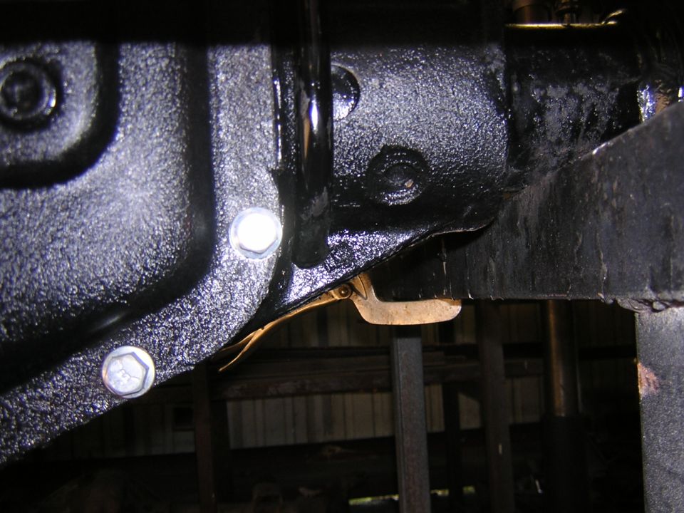 Underside view of glossy black-painted drivetrain components with two silver hex bolts on a Ford F-250 in a shop.