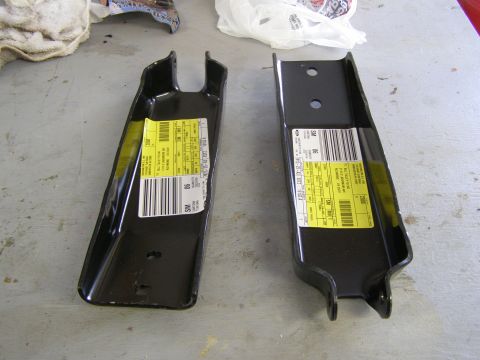 1993 Ford Bronco - Two black metal automotive parts with yellow labels and barcodes are laid out on a gray surface.