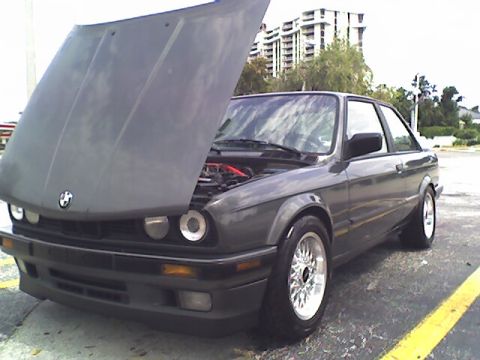 1989 BMW 3 Series - This BMW E30 coupe is shown with its hood open, revealing the engine compartment and aftermarket wheels.