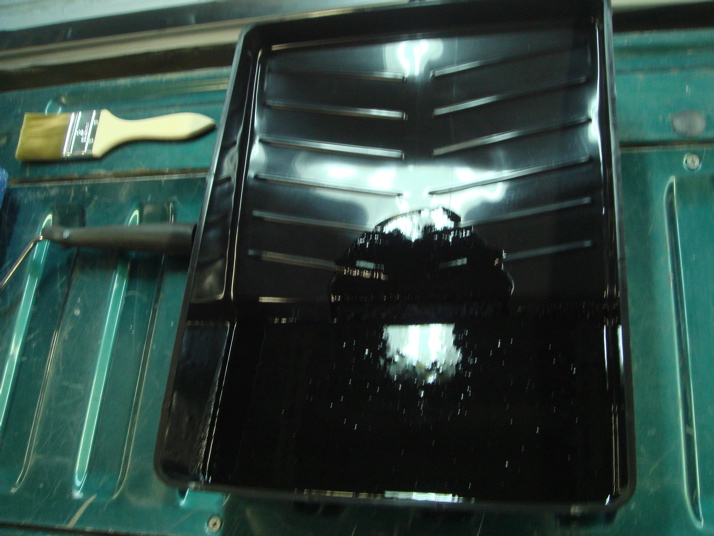 Paint tray with black paint, roller, and brush on a green surface