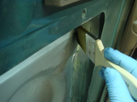 1996 Ford Bronco - A gloved hand uses a brush to apply a substance to the interior of a vehicle door panel.