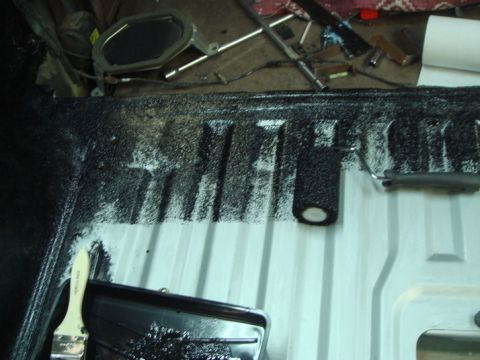 1996 Ford Bronco - A vehicle's interior floor is being coated with a black protective material using a brush and roller.