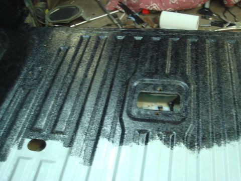 1996 Ford Bronco - Close-up of a truck bed liner being coated with a black textured material.