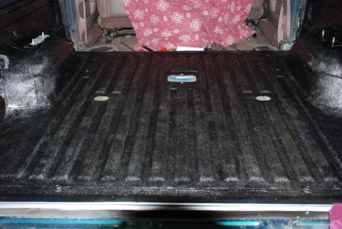 1996 Ford Bronco - The interior of a truck bed shows a freshly applied black textured liner.