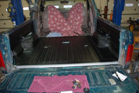 1996 Ford Bronco - Rear view of a teal pickup truck bed a black spray-in liner and patterned seat covers, with a vehicle lift visible in the background.