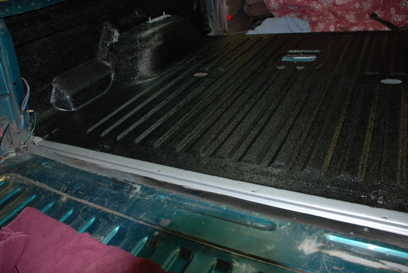 SUV rear cargo floor coated in black spray-in bedliner viewed over open teal tailgate