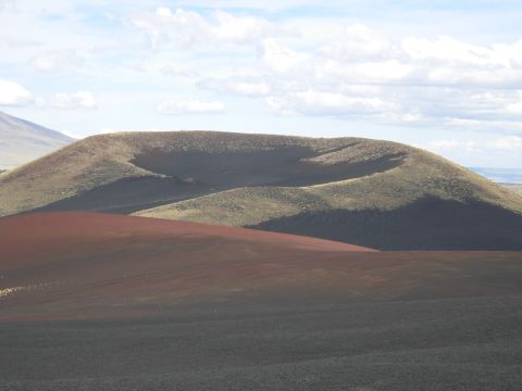 1986 Ford Bronco - A scenic view of a volcanic landscape rolling hills of red and dark gray soil under a partly cloudy sky.