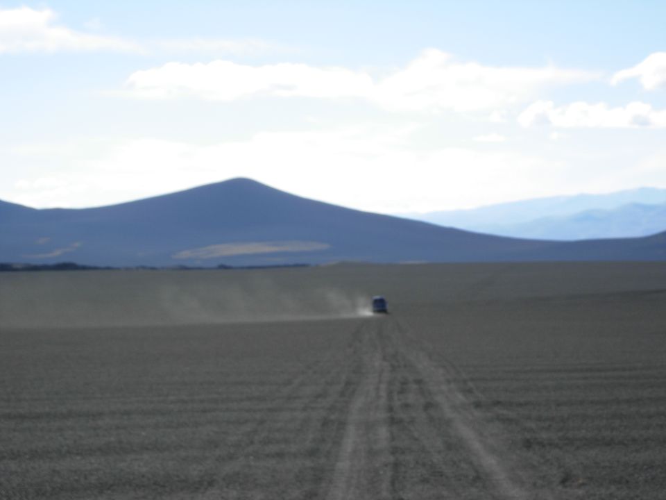 Vehicle driving on a dirt road in a desert landscape with mountains in the background