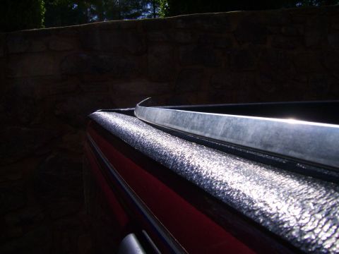 1982 Ford Crown Victoria LTD - Close-up view of a red pickup truck's bed rail, textured black spray-on liner and a polished chrome trim piece.