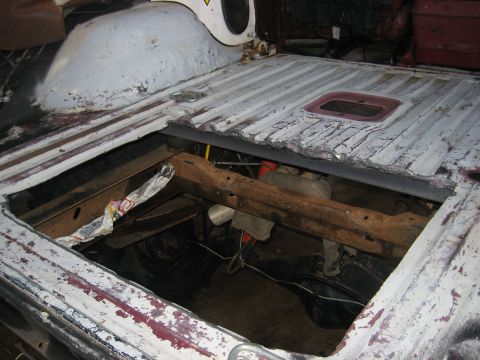 1979 Ford Bronco - The exposed undercarriage of a vehicle reveals rusted frame and suspension parts through a hole in the bed.