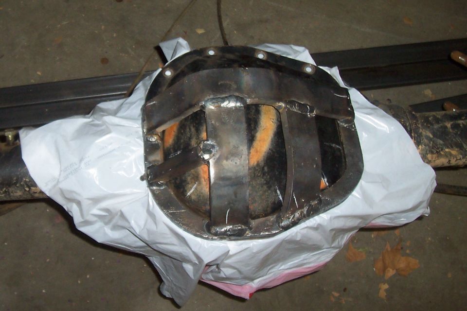 Differential cover with welded metal reinforcement plates, partially covered by white plastic