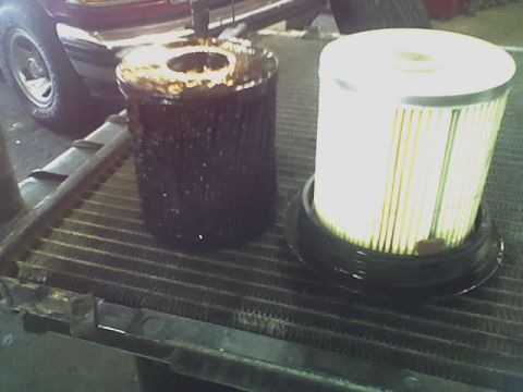 1992 Ford Bronco - Comparing a used oil filter with a new one, placed on a car's radiator.