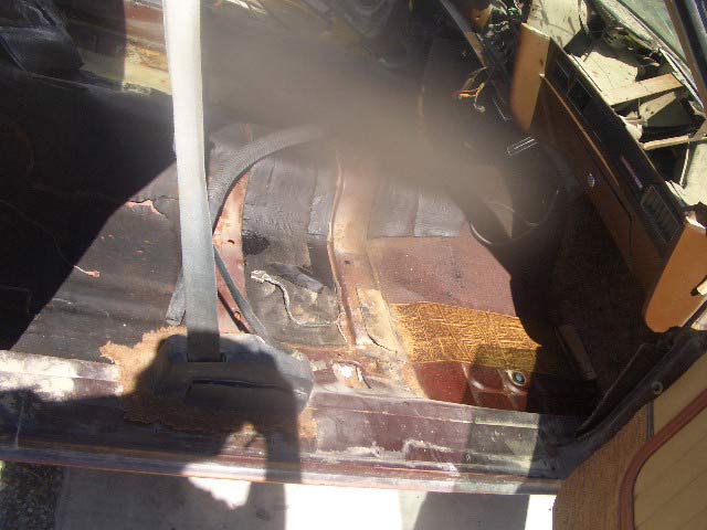 Vehicle interior floor pan with heavy rust and worn flooring near door sill