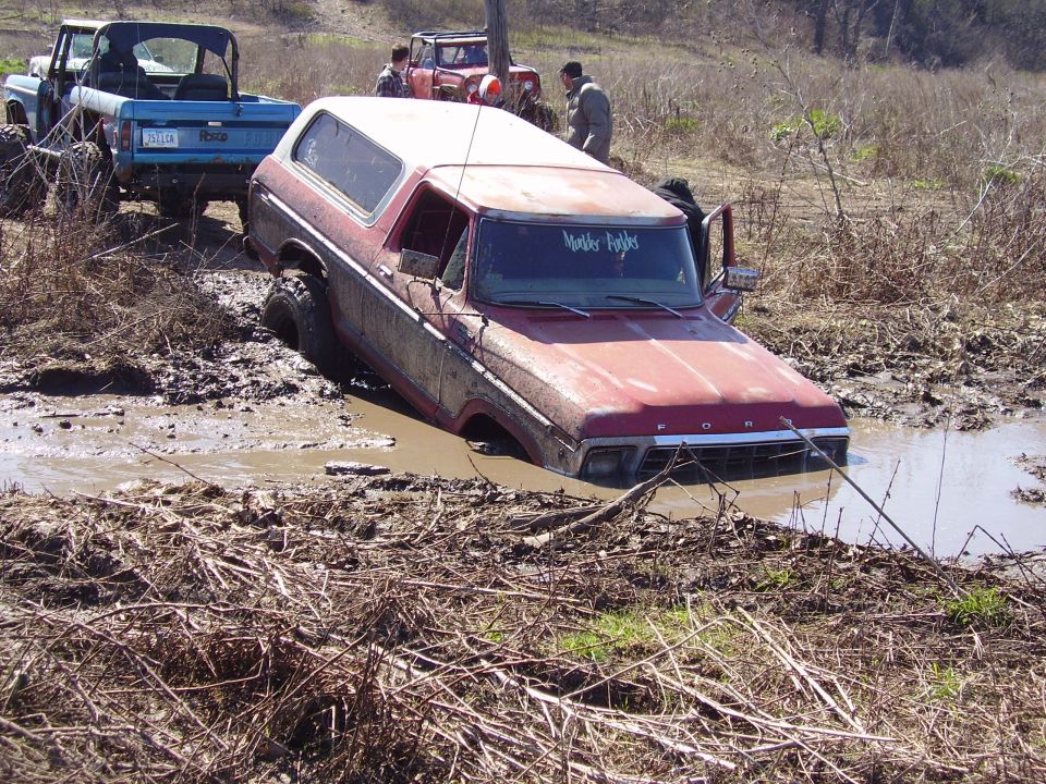 Red Ford Bronco stuck in mud, front grille visible, "Mother F***ers" sticker on windshield