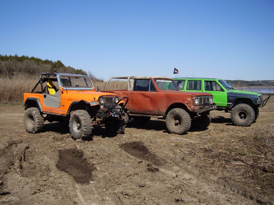 Orange Jeep CJ, rusty Scout and green wagon parked on dirt