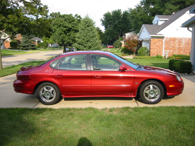 Maroon Ford Taurus sedan parked sideways in a suburban driveway with chrome wheels