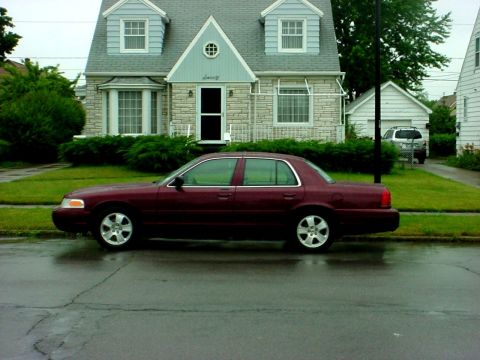 1989 Ford Taurus - A maroon sedan is parked on a wet street in front of a house.