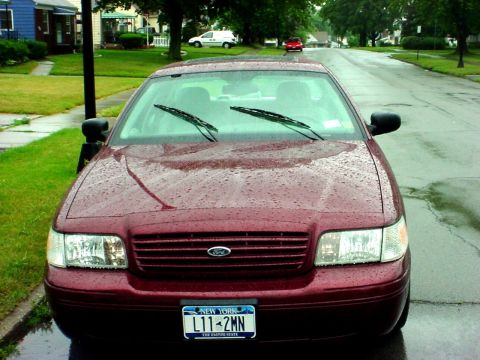 1989 Ford Taurus - Maroon Ford Crown Victoria parked on a residential street in the rain, showing its front grille and headlights.