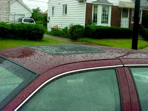 1989 Ford Taurus - The photo shows the roof of a car with a sunroof, wet from rain, with a house and another vehicle in the background.