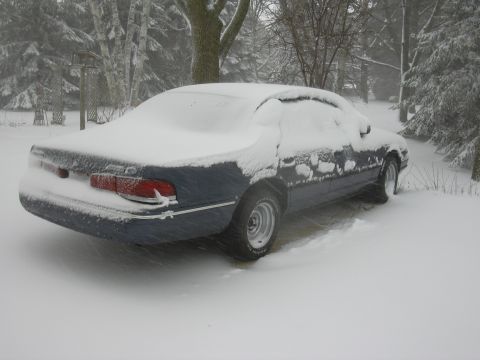 1996 Ford Crown Victoria - A dark blue sedan sits covered in snow during a winter storm.
