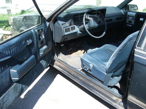 1991 Ford LTD Crown Victoria - The interior of a car shows blue fabric seats and a dark dashboard with the driver's side door open.