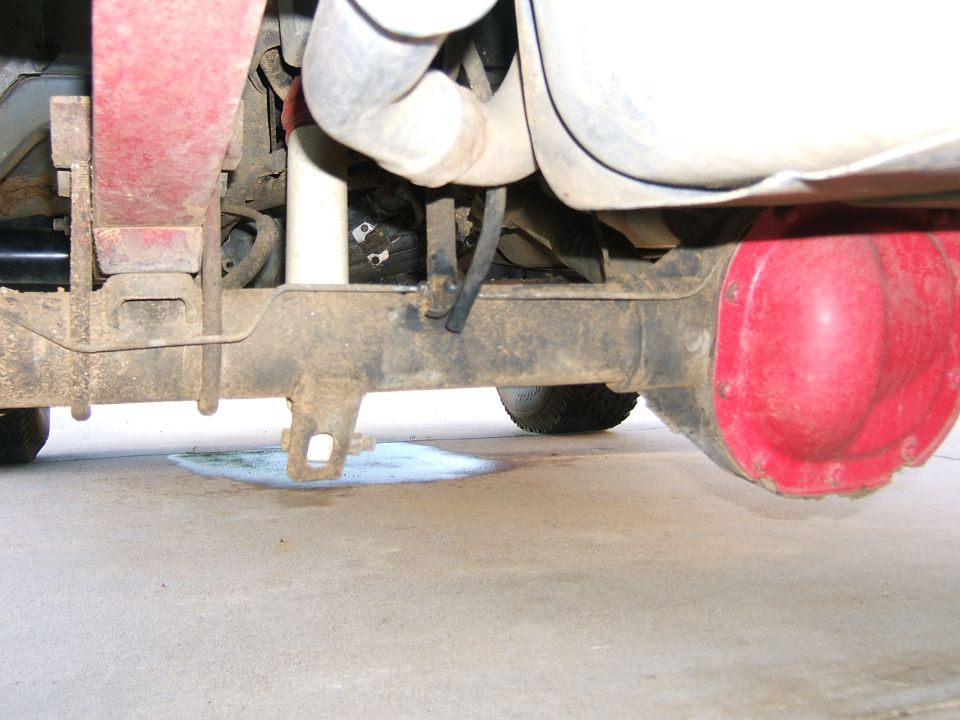 Red differential housing on a vehicle's rear axle with leaf springs and exhaust pipe visible