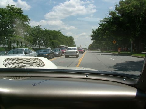 1972 Ford Ranchero - A white sedan drives in traffic on a sunny day, with trees lining the road.
