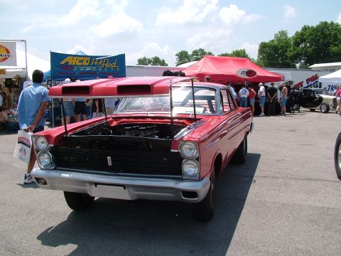 1972 Ford Ranchero - A red custom coupe with its hood open, displaying the engine, at an outdoor event with tents and spectators.