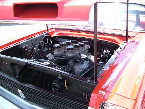 1972 Ford Ranchero - Engine bay of a red car, showing a V8 engine with multiple carburetors and a prominent hood scoop.