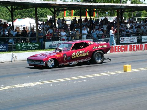 1972 Ford Ranchero - A modified red drag car with custom graphics races down the track in front of a crowd.