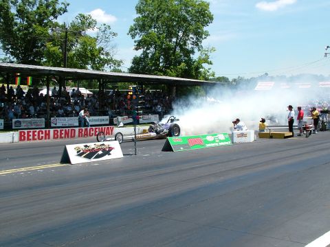 1972 Ford Ranchero - A dragster emits a large cloud of smoke as it races down the track at Beech Bend Raceway, with spectators in the background.