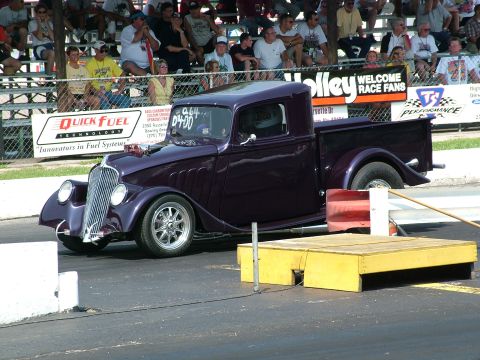 1972 Ford Ranchero - A custom purple pickup truck sits on a drag strip with spectators watching from the stands.