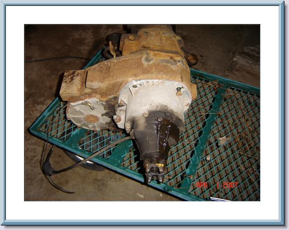 Rusty cast iron transfer case with output yoke sitting on a green metal grate