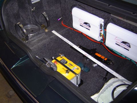 1995 Ford Thunderbird - The trunk of a car contains two white audio amplifiers, a yellow battery, and a measuring tape.