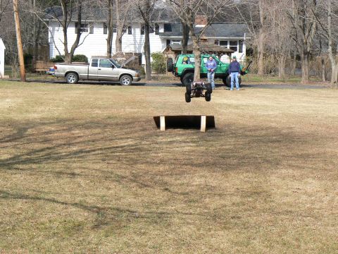 1994 Ford Bronco - RC buggy jumps a ramp in a yard with a pickup truck and SUV present.