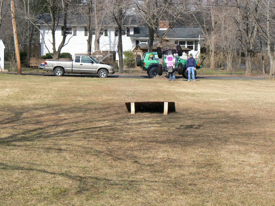 green Jeep flipped on its side with two people standing nearby; silver pickup truck parked in background