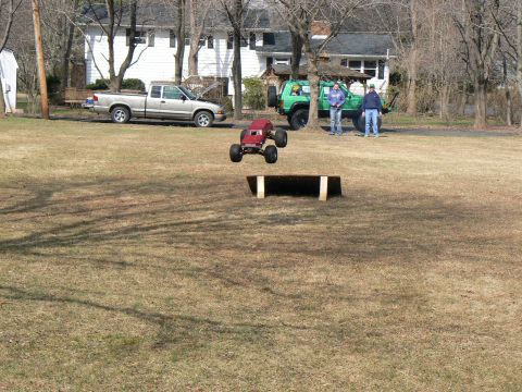 1994 Ford Bronco - A remote control monster truck soars through the air after launching off a wooden ramp in a grassy yard.