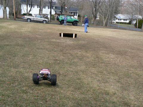 1994 Ford Bronco - A remote control monster truck is in the foreground on a grassy field, with two full-size vehicles and people in the background.