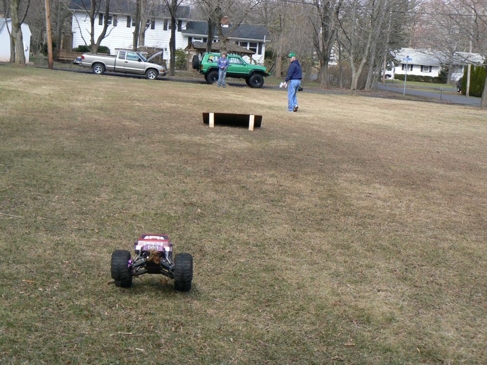 RC monster truck on grass, with a pickup truck and green SUV in background