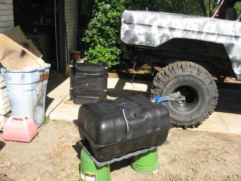 1979 Ford Bronco - A Ford Bronco in primer with a new fuel tank and large tires sits outside a garage.