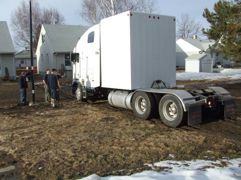 1990 Ford Bronco - Semi-truck and trailer parked on muddy terrain with houses in the background.