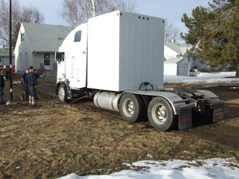 1990 Ford Bronco - A white semi-trailer truck is parked on a muddy lot with some snow on the ground.