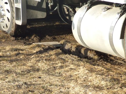 1990 Ford Bronco - A large truck's fuel tank and wheel are visible, partially sunk into muddy ground.