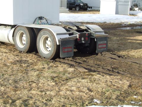 1990 Ford Bronco - Semi-truck rear wheels stuck in muddy yard with a black SUV in the background.