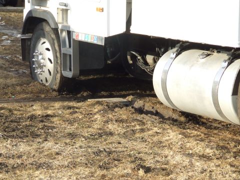 1990 Ford Bronco - A semi-truck's front tire is stuck in muddy terrain.